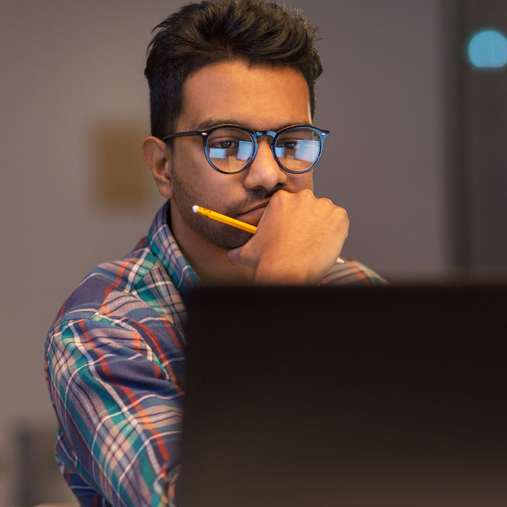 A man with eyeglasses staring at his laptop monitor.